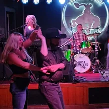A man in a cowboy hat and a woman dancing together in front of a live band playing on stage at a bar